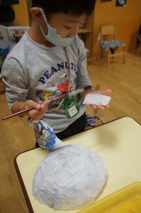 年長組・・・はりぼてのお面を製作中です。新聞紙と和紙を風船の上に何度も重ねて貼り付けています。